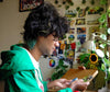 Person in a green jacket sitting at a desk working with art prints, cutting with punch cutter